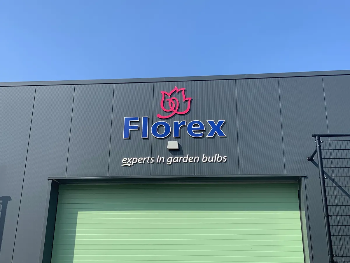 Florex-logo met de tekst experts in garden bulbs op de grijze gevel boven een groene roldeur