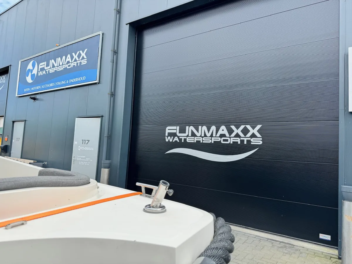 Logo FUNMAXX WATERSPORTS op de donkere roldeur, met een boot op de voorgrond