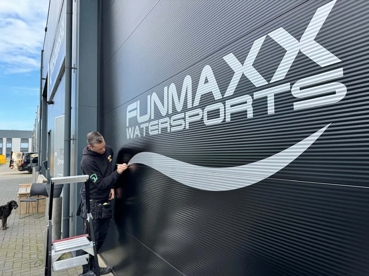 Monteur werkt de grote belettering FUNMAXX WATERSPORTS af op de gevel