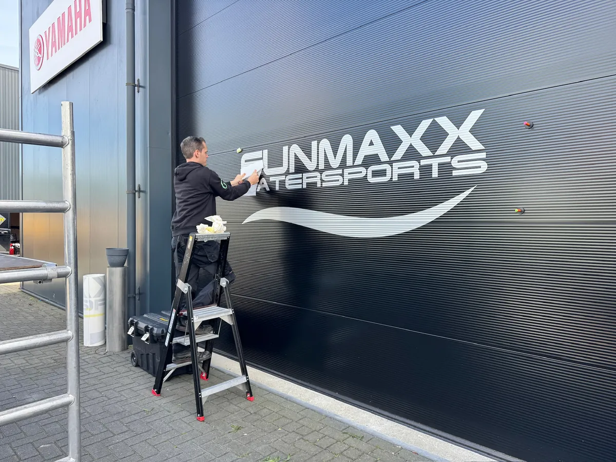 Monteur op een trapje werkt de belettering FUNMAXX WATERSPORTS af
