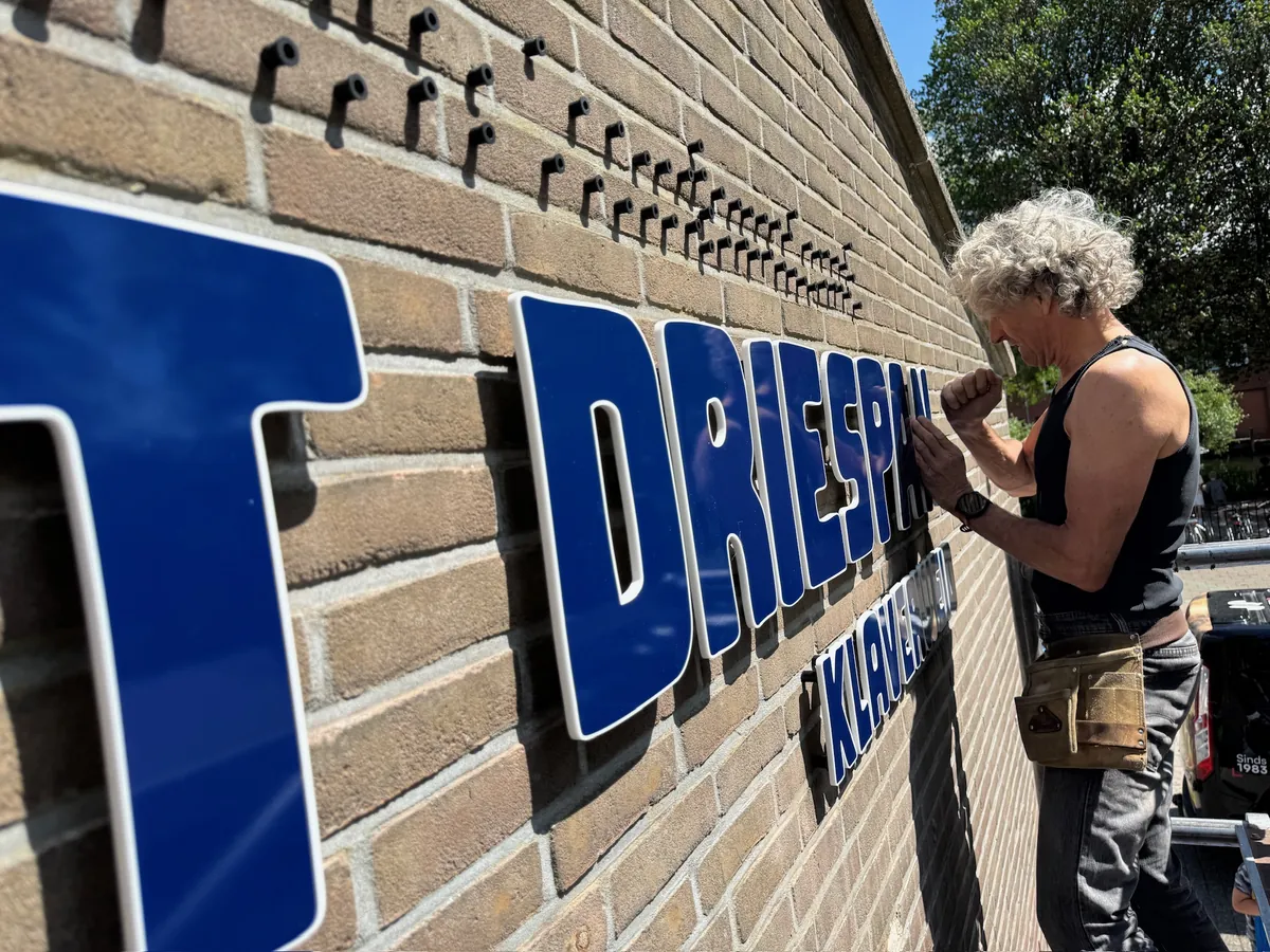 Monteur bevestigt de grote blauwe letters HET DRIESPAN op de bakstenen gevel