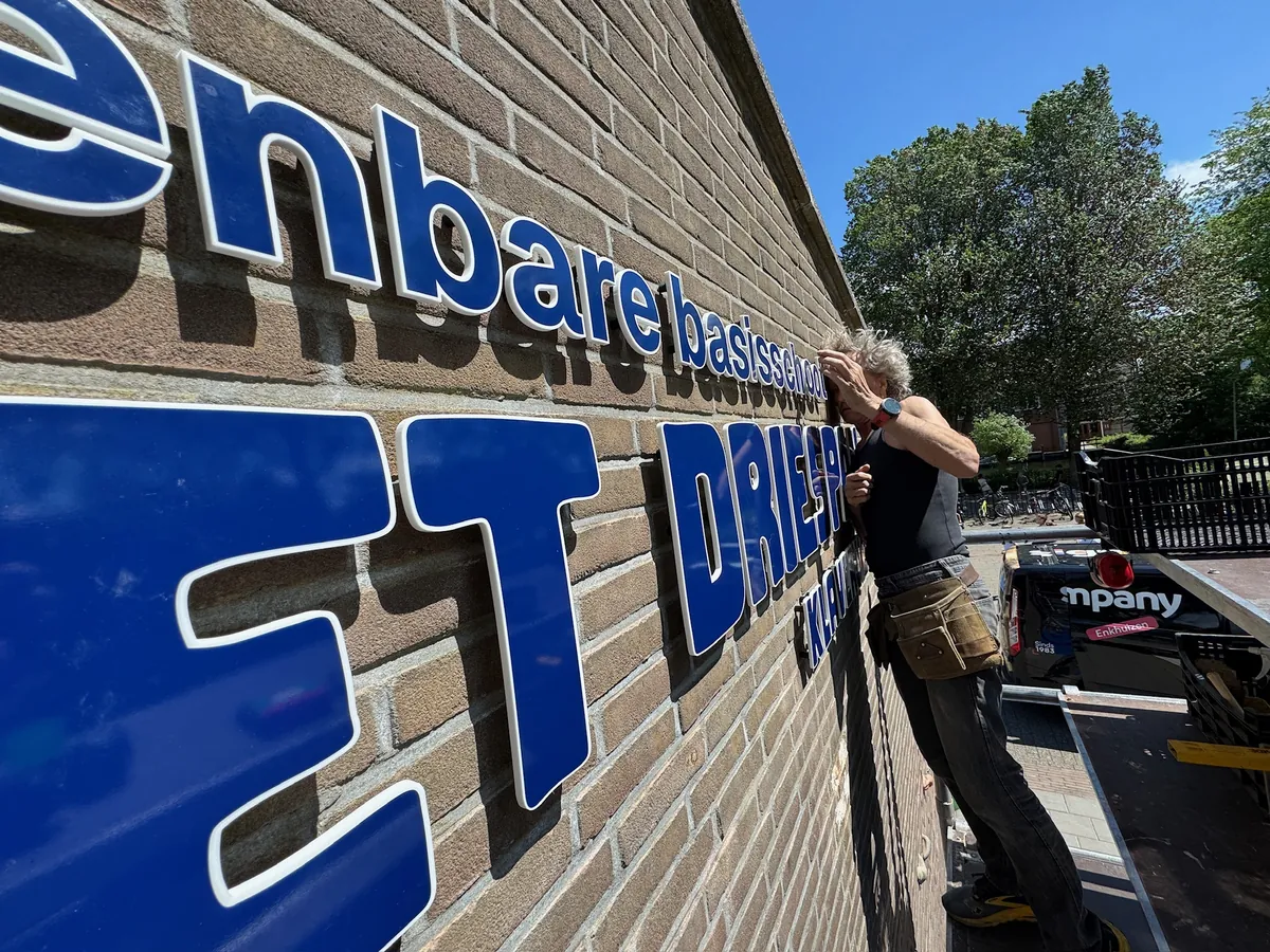 Monteur zet de blauwe letters van Het Driespan vast op de baksteen
