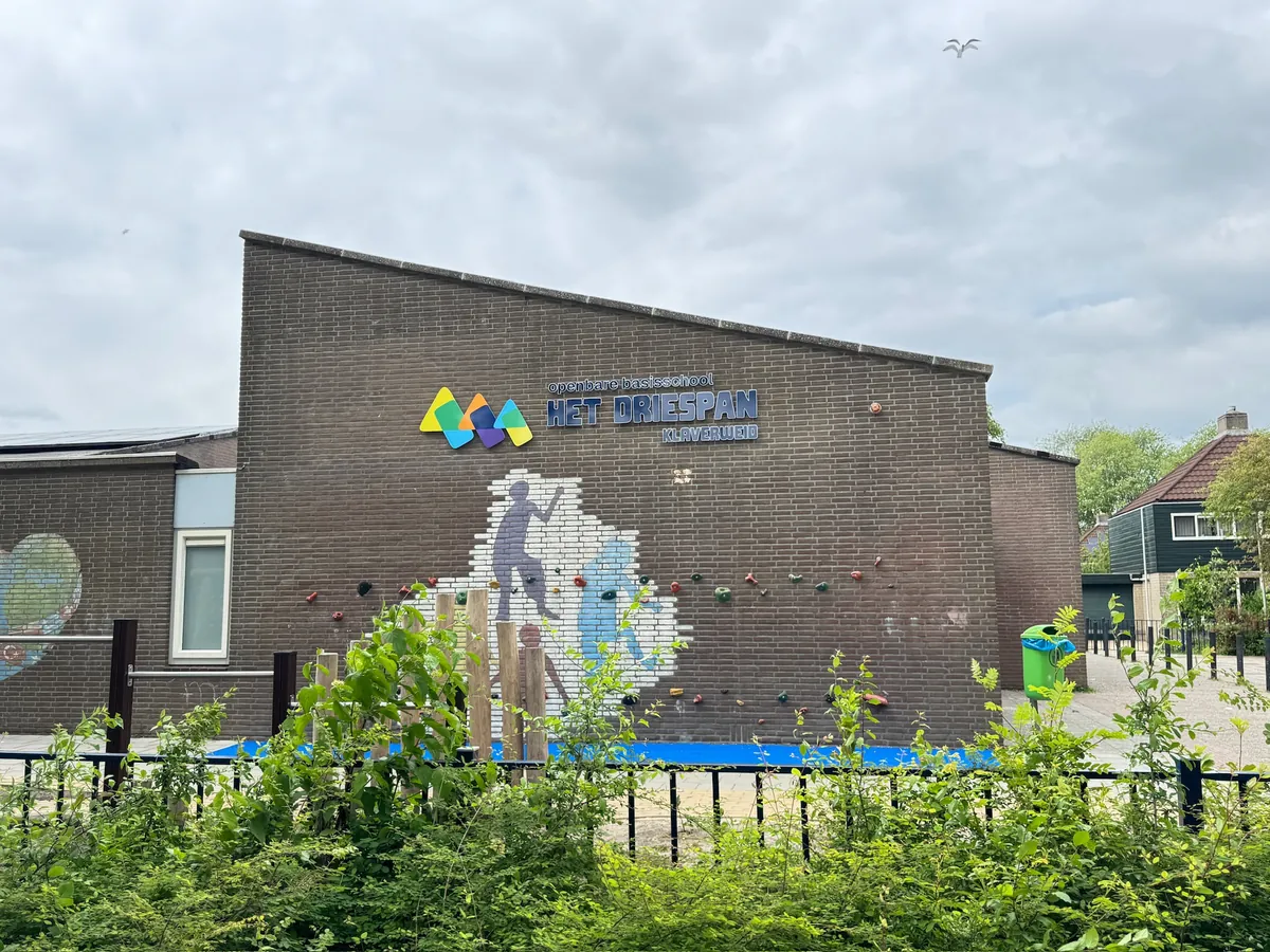Bakstenen muur met logo en klimvlak, gezien vanaf het schoolplein