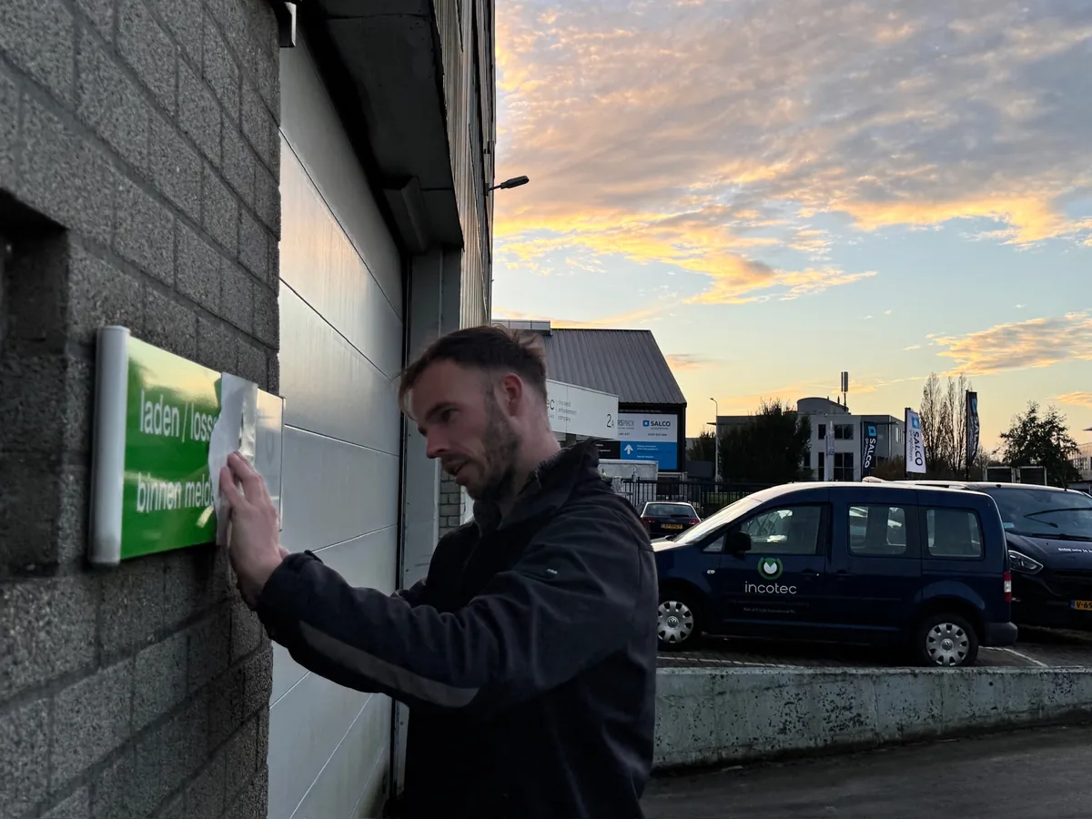 Monteur bevestigt een groen bord voor laden en lossen op de gevel, bij zonsondergang