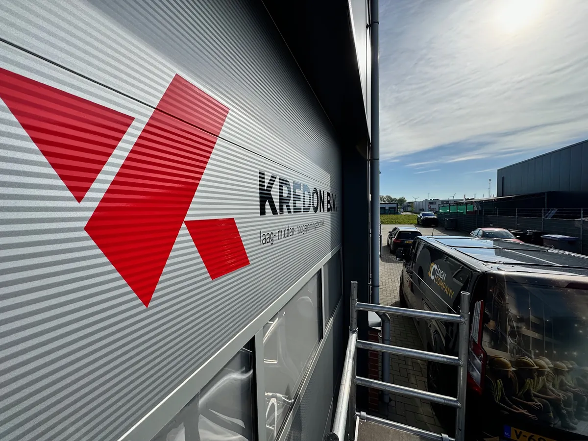 Rood Kredon-beeldmerk en naam op de lichtgrijze gevel, van dichtbij