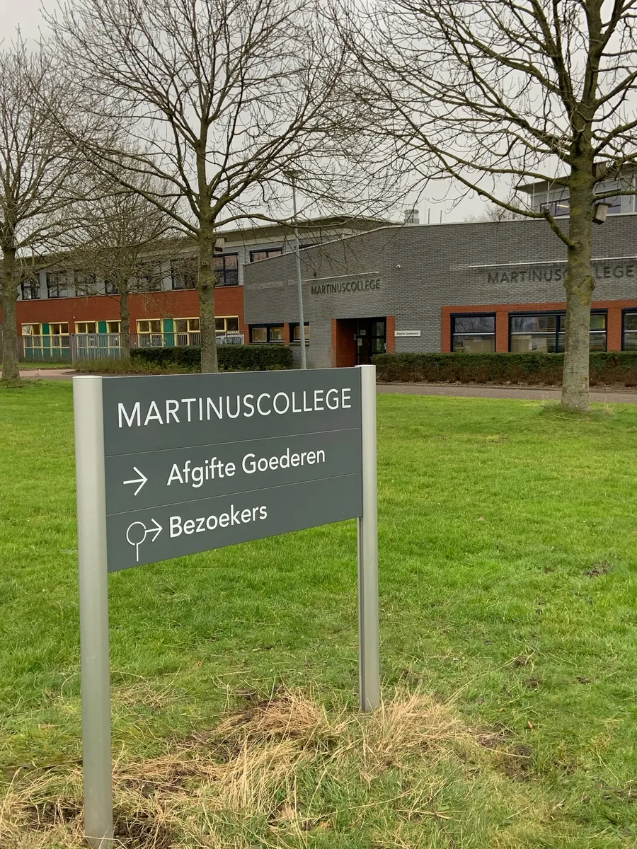 Grijs bord Martinuscollege met pijlen naar afgifte goederen en bezoekers