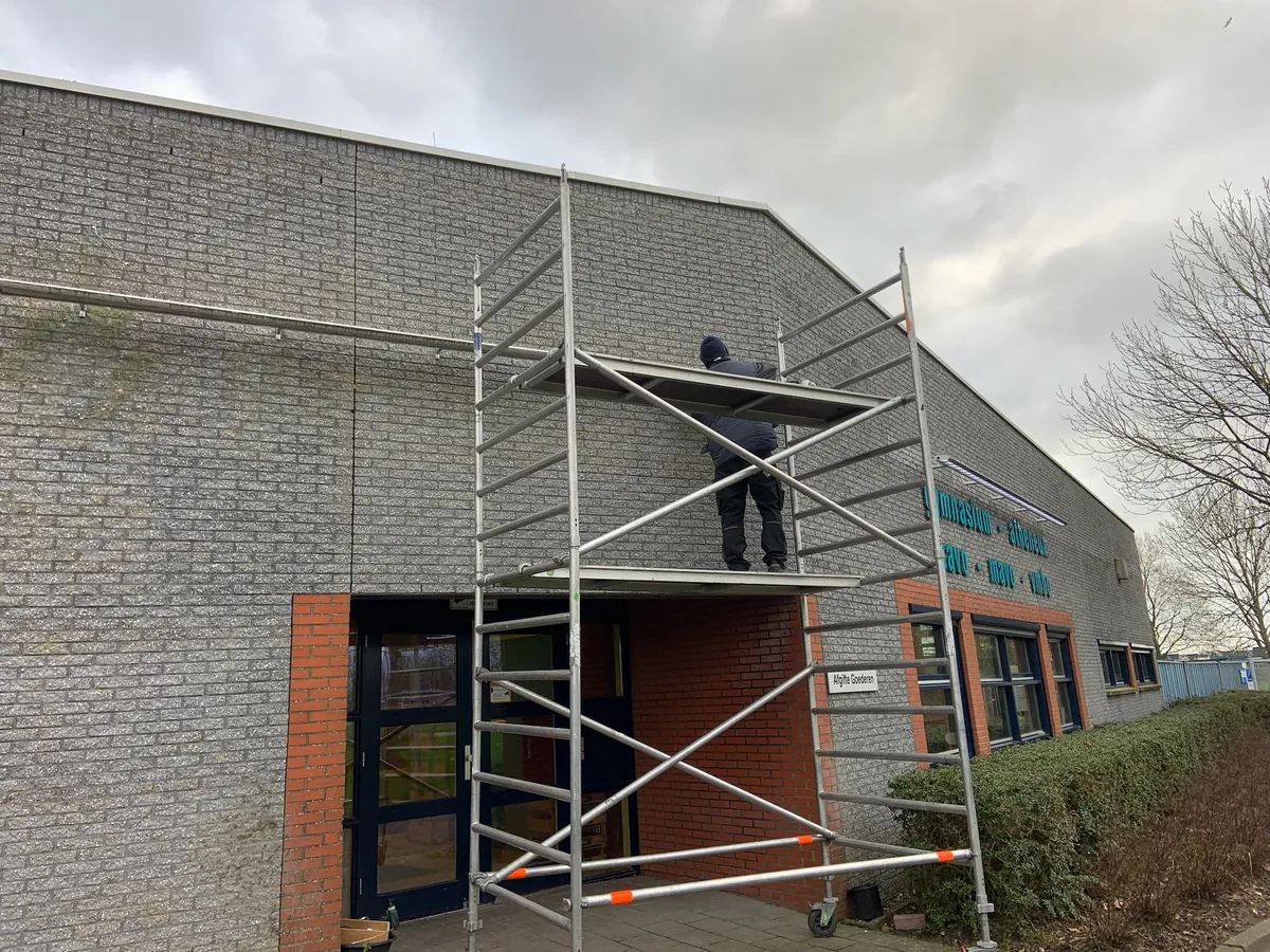 Monteur op een steiger bij de gevel boven de entree van het Martinuscollege