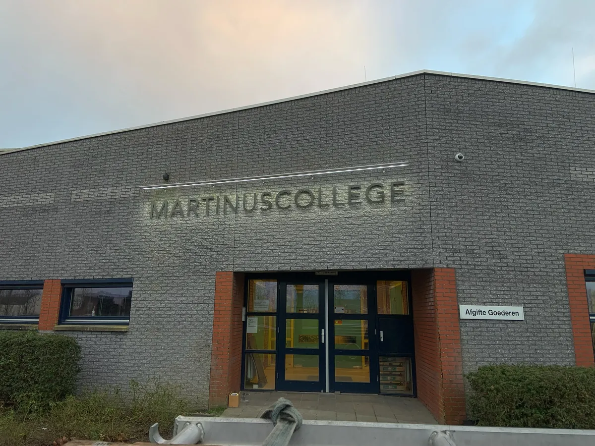 Letters MARTINUSCOLLEGE op de grijze bakstenen gevel boven de entree