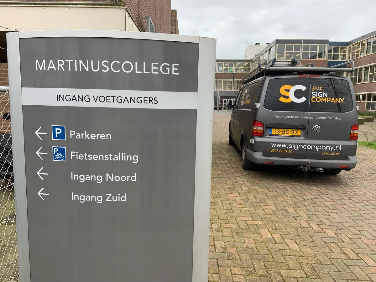 Grijs richtingbord van het Martinuscollege met pijlen naar parkeren, fietsenstalling en de ingangen