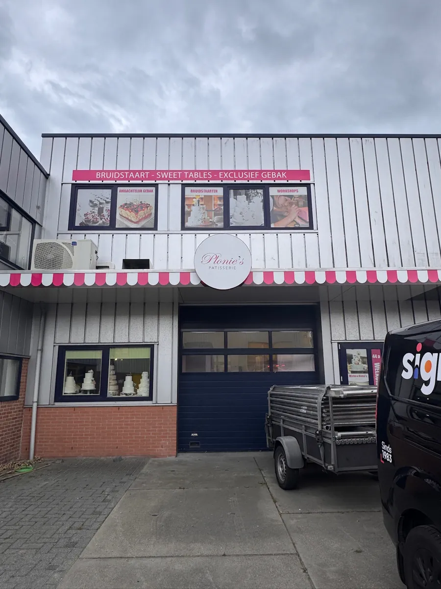 Gevel met het ronde bord van Plonie's Patisserie boven de roze-witte zonwering