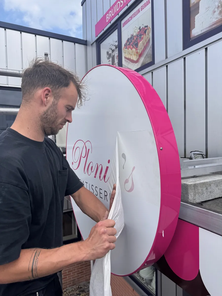 Monteur trekt de beschermfolie van het ronde roze-witte bord van Plonie's Patisserie