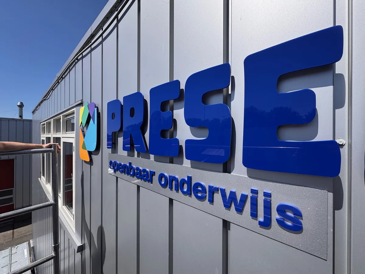 Blauwe letters PRESENT en de tekst openbaar onderwijs op de grijze gevel