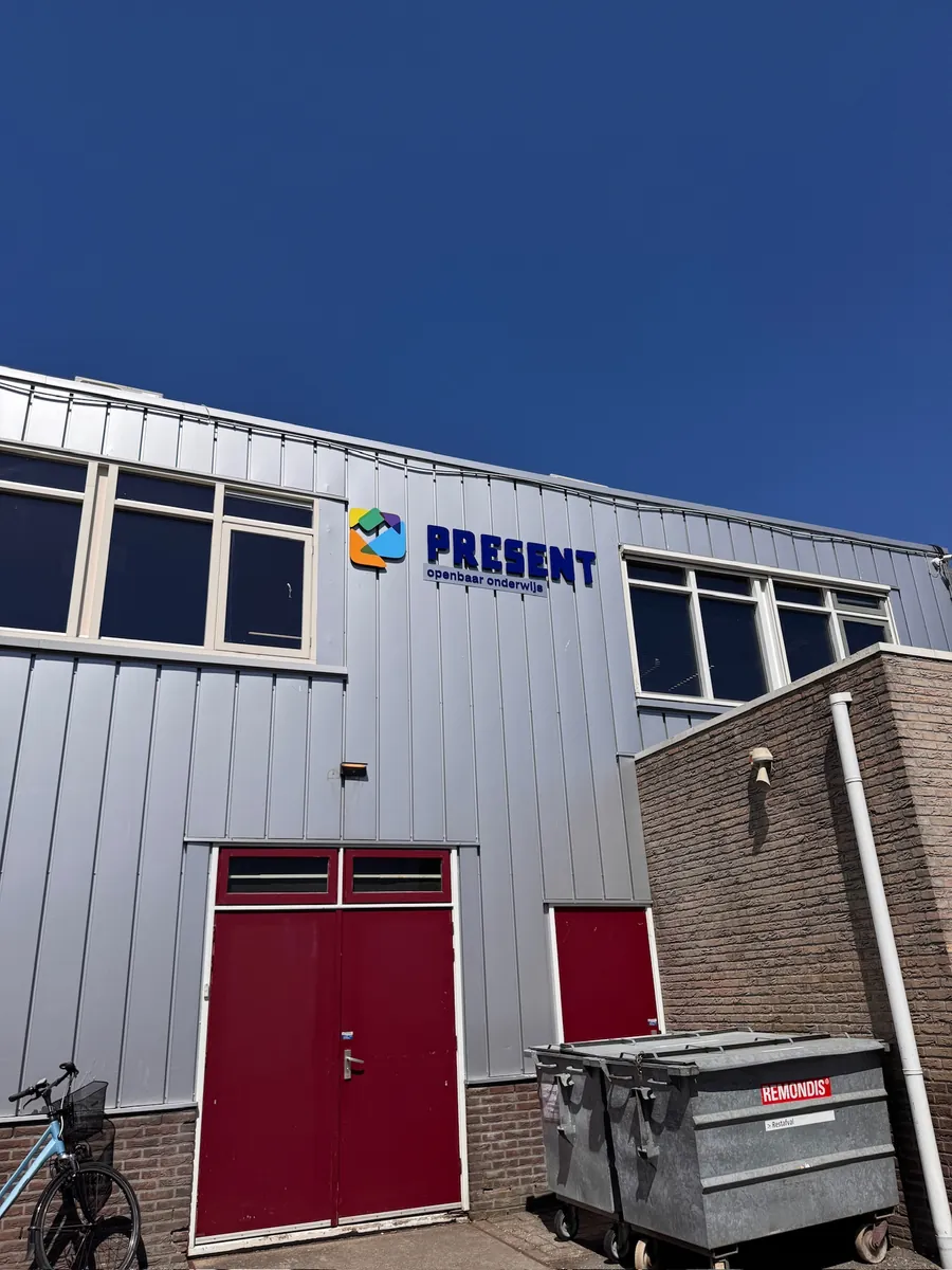 Gevel van het schoolgebouw met het Present-logo boven rode deuren