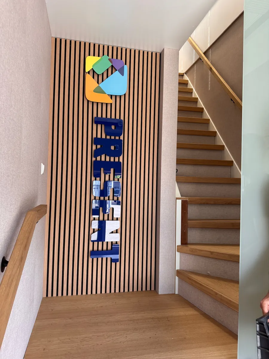 Lamellenwand bij de trap met logo en verticale blauwe letters PRESENT