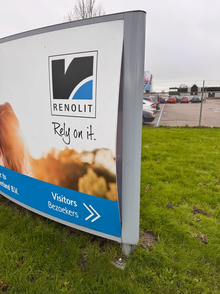 Gebogen bord van Renolit met een blauwe pijl voor bezoekers, op het gras