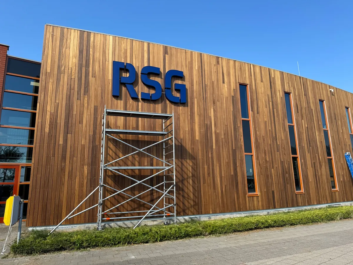 Blauwe letters RSG op de gebogen houten gevel onder een blauwe lucht
