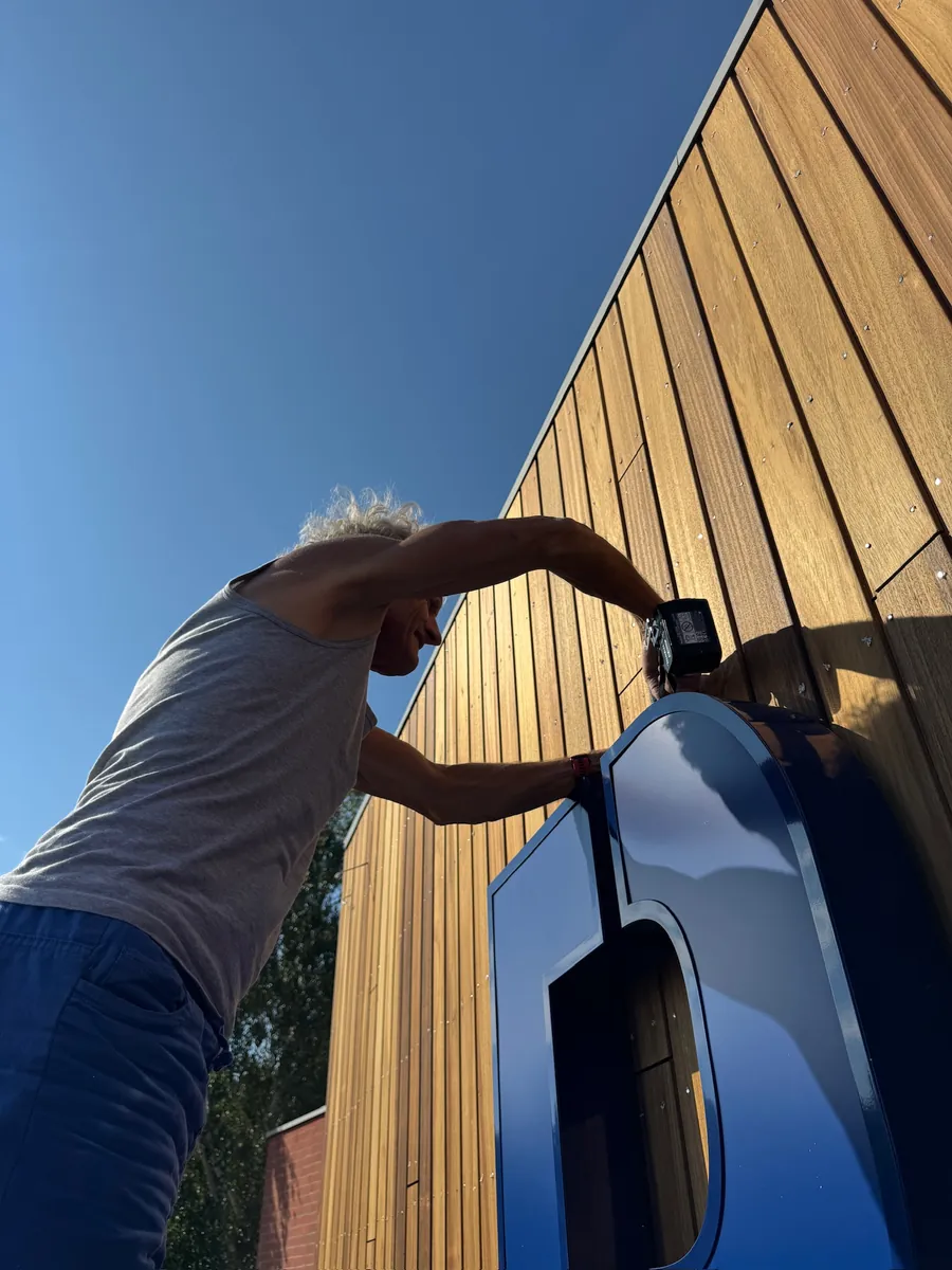 Monteur zet een blauwe letter vast op de houten gevellatten
