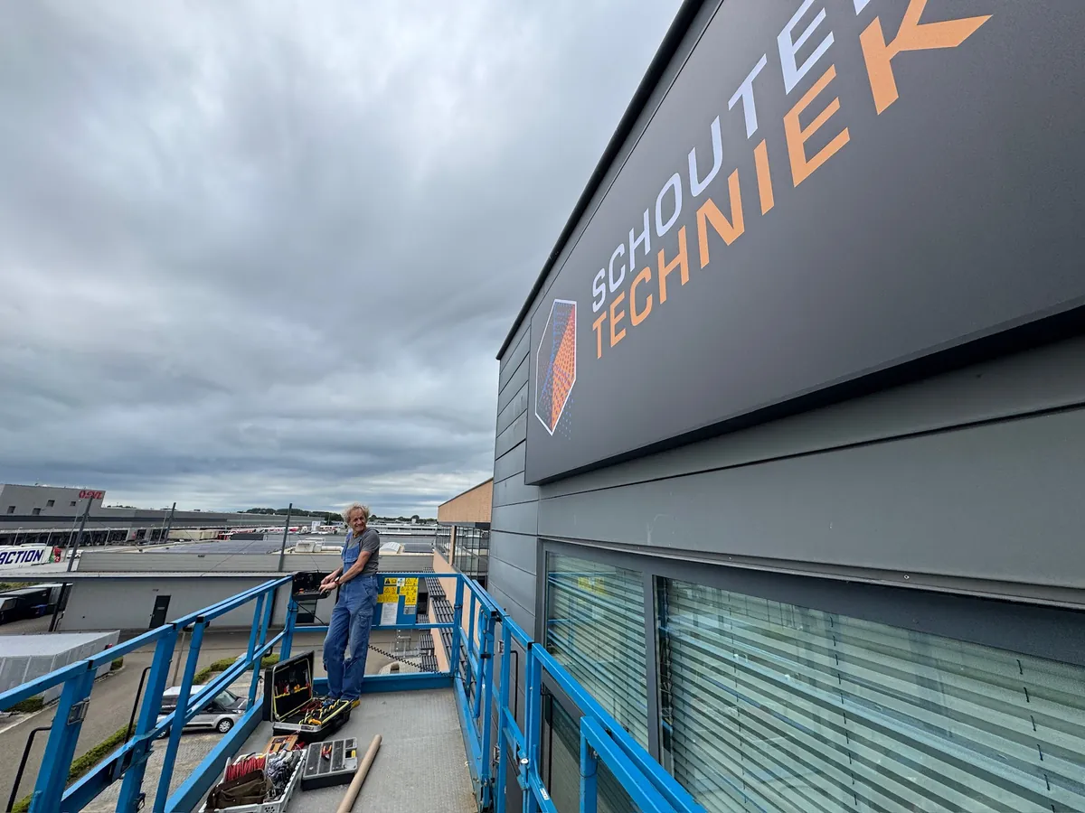 Monteur op de hoogwerker onder het bord met Schouten Techniek