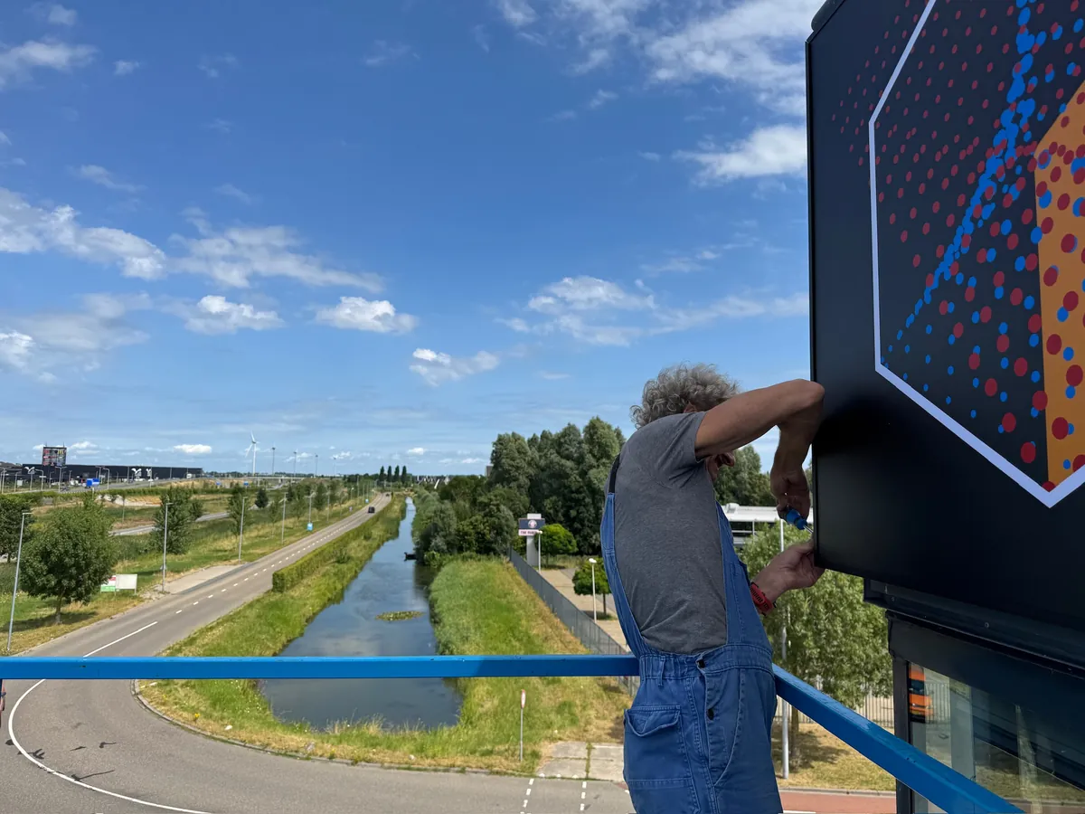 Monteur op de hoogwerker bevestigt het bord, met uitzicht over een vaart
