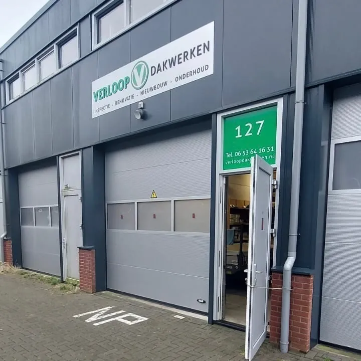 Wit gevelbord van Verloop Dakwerken boven de roldeur en een groen deurpaneel met huisnummer 127