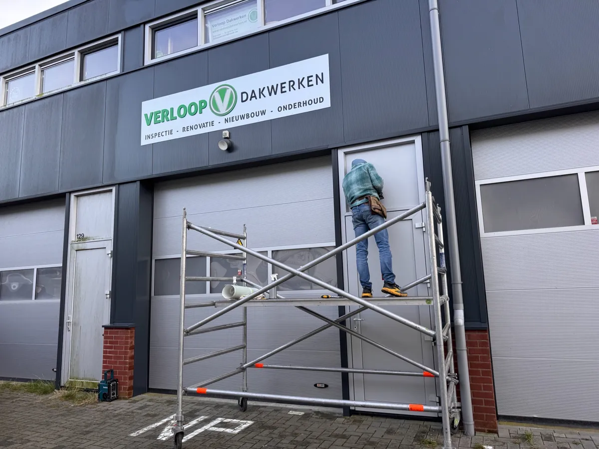 Monteur op een rolsteiger bij de deur onder het gevelbord van Verloop Dakwerken