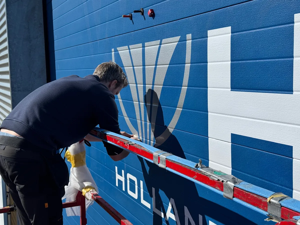 Monteur met een lat bij het HJB-beeldmerk op de roldeur