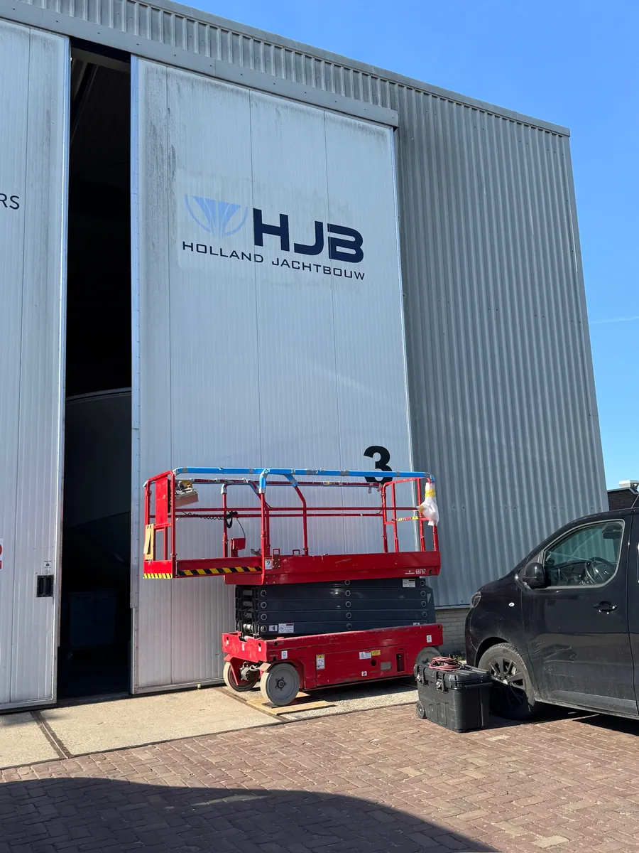Grijze schuifdeur met het HJB-logo en een hoogwerker ervoor