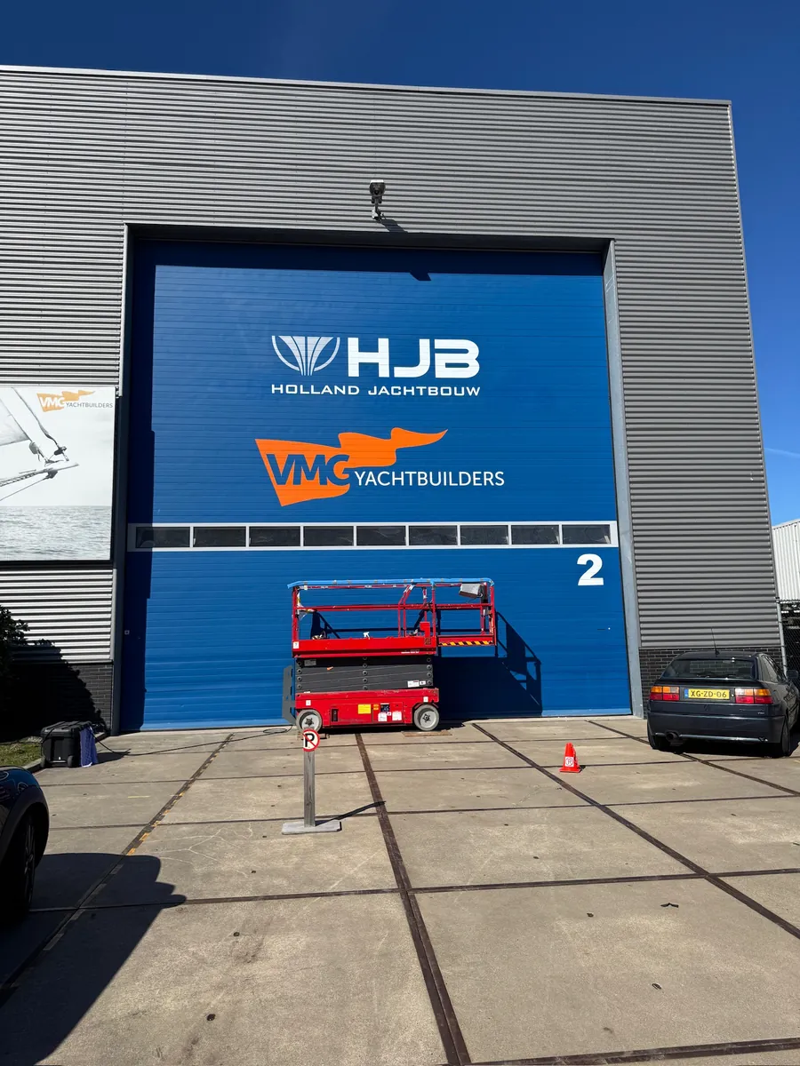 Blauwe roldeur met de logo's HJB Holland Jachtbouw en VMG Yachtbuilders