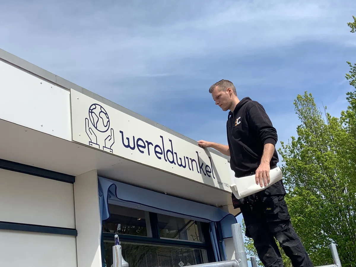 Monteur plakt de letters wereldwinkel op de witte gevelrand