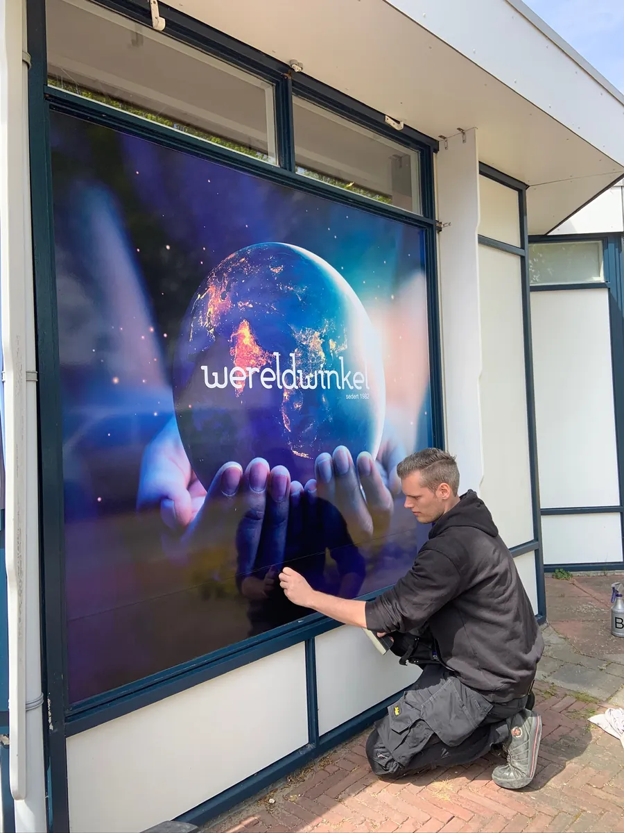 Monteur brengt een raambeeld met een wereldbol in handen aan op het winkelraam