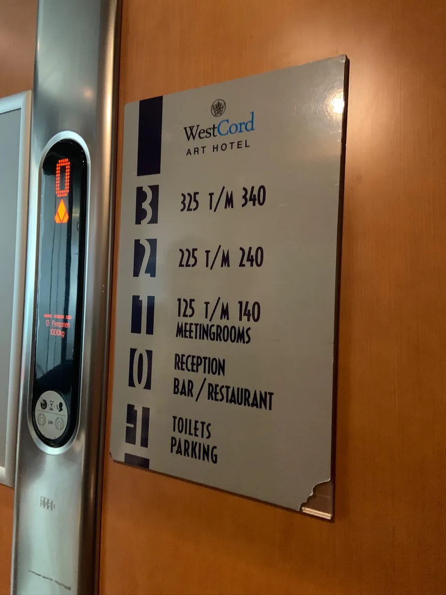 Metalen verdiepingenbord van WestCord Art Hotel naast de lift