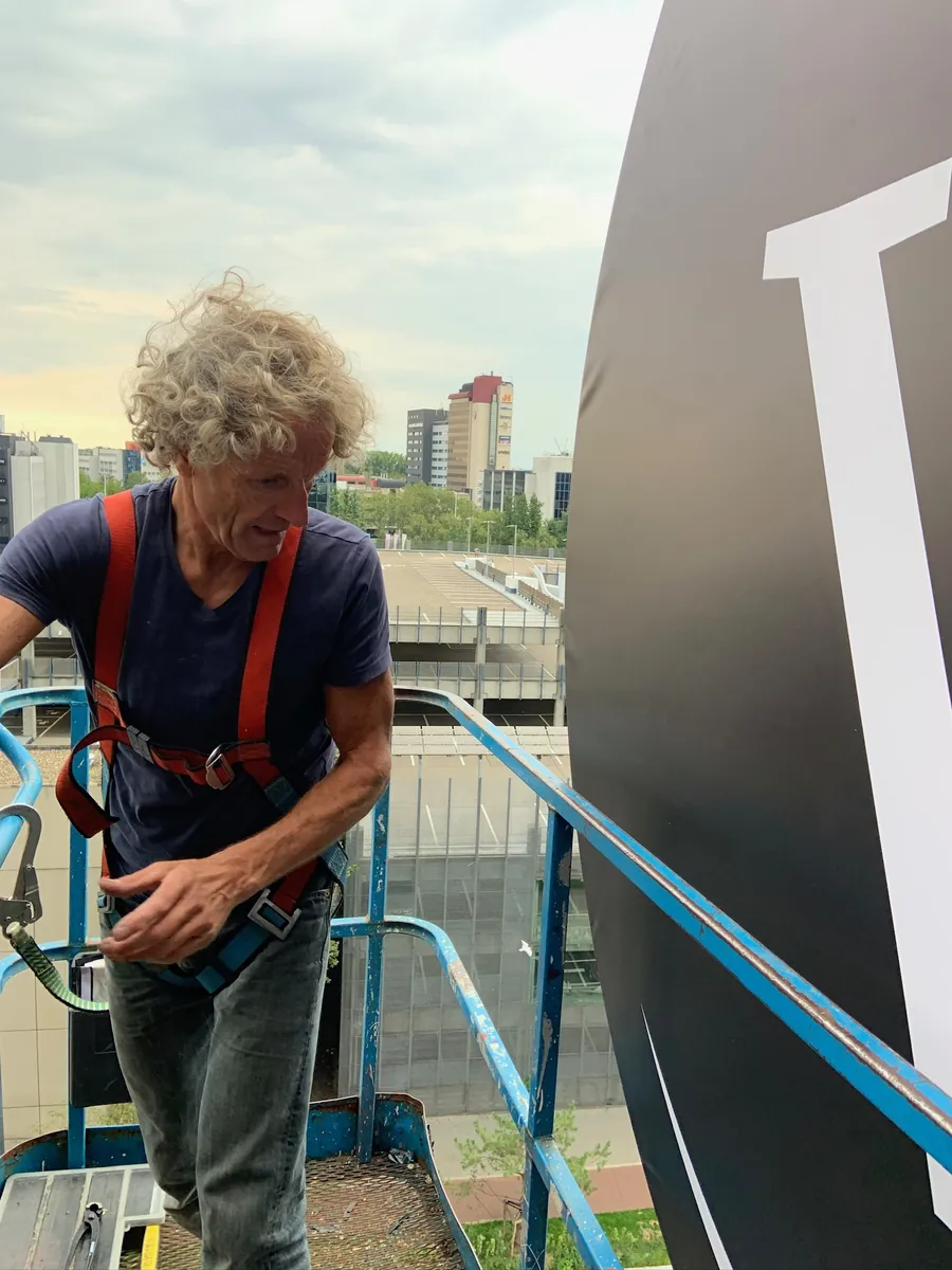 Monteur in harnas op een hoogwerker naast de grote witte W op de gevel