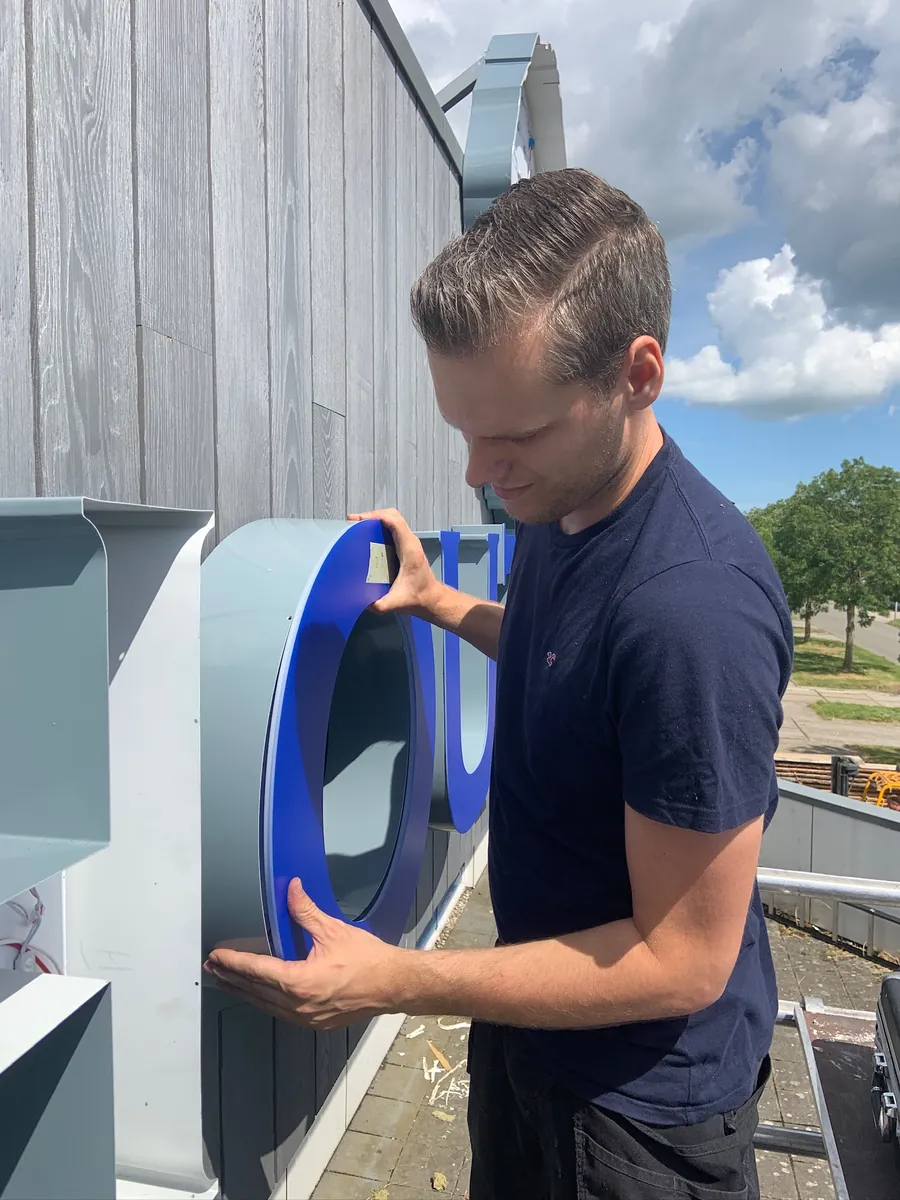 Monteur houdt de blauwe letter O vast bij de gevel