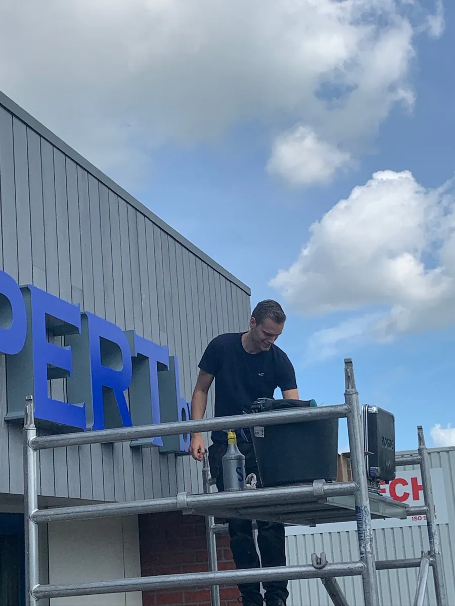 Monteur op de steiger bij de blauwe letters van Hout Expert
