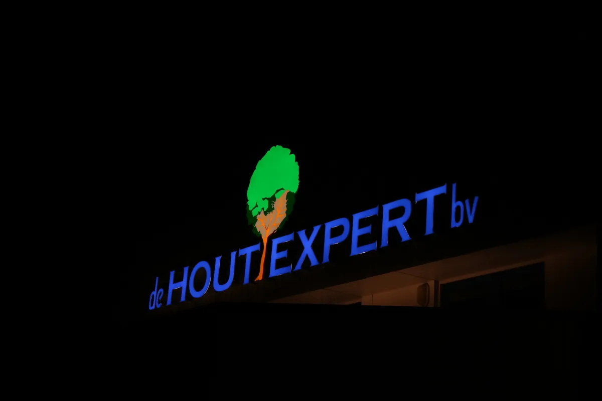 Verlichte letters de Hout Expert met boomlogo bij nacht, schuin gezien