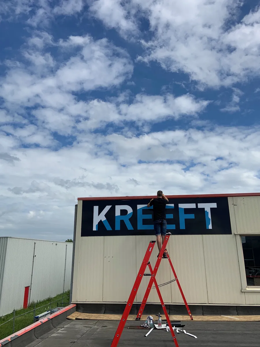 Zwart gevelbord met KREEFT met een monteur op een rode trap