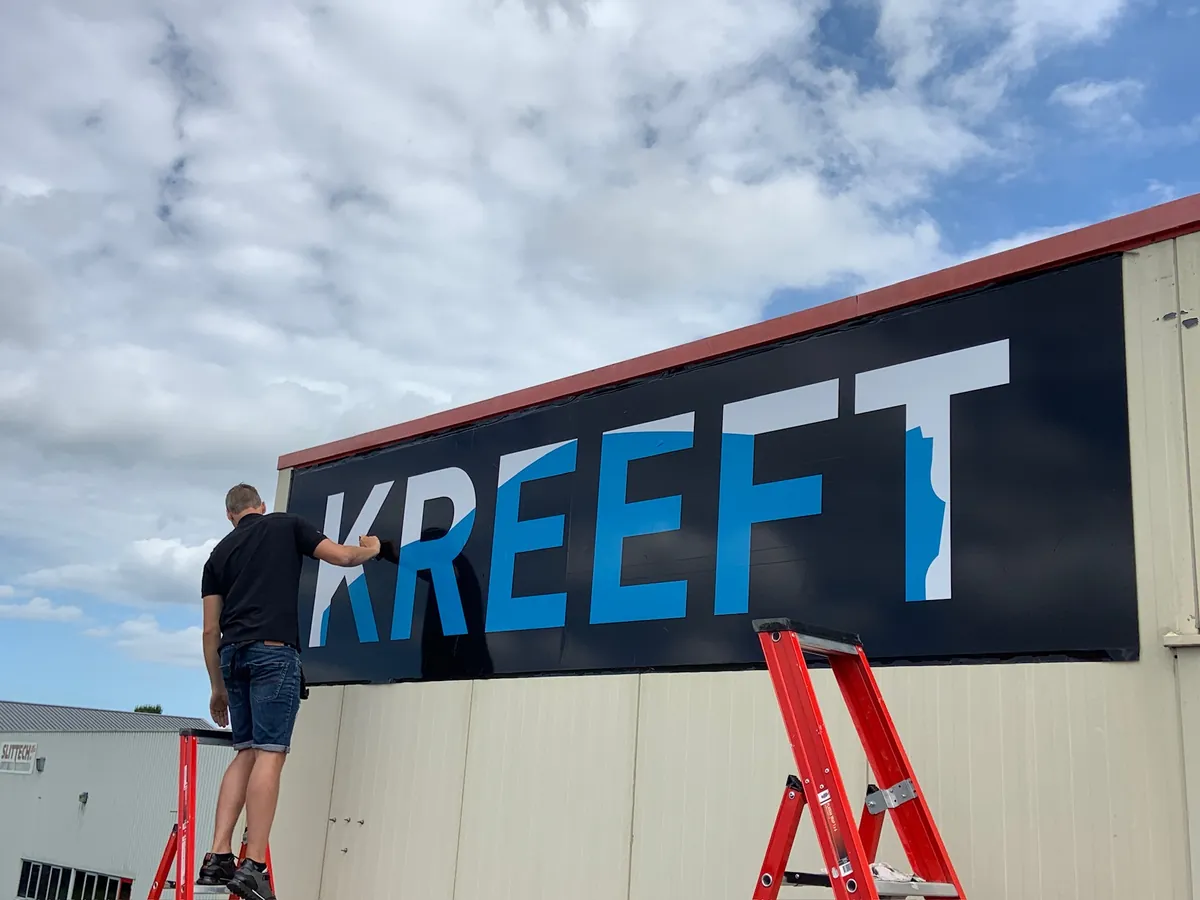 Monteur op een trapje werkt het zwarte gevelbord met KREEFT af