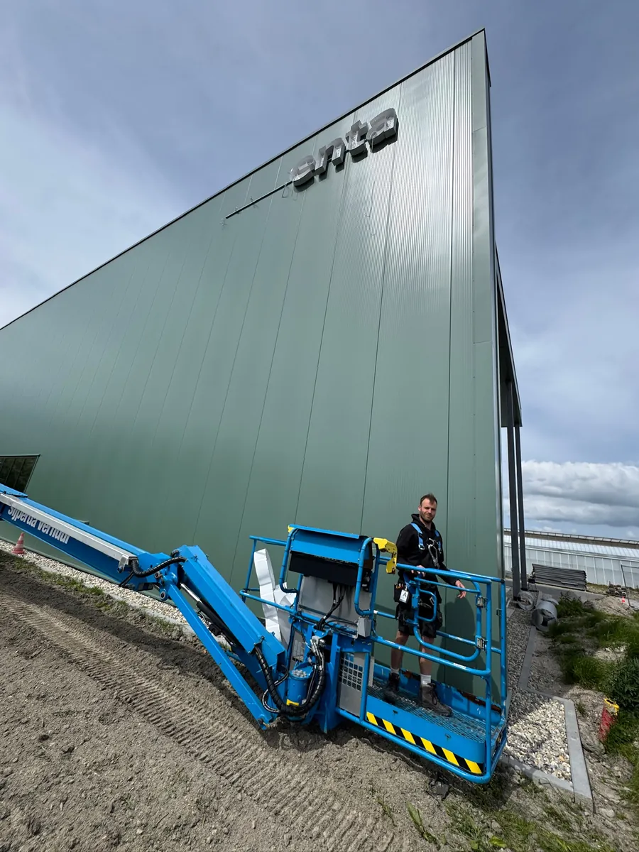 Hoogwerker met monteur onder de hoge groene gevel
