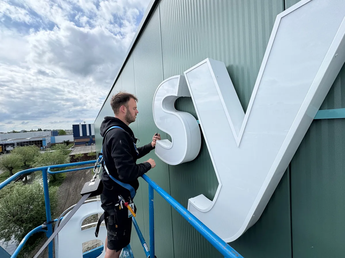 Monteur op de hoogwerker naast de grote witte letters s en y
