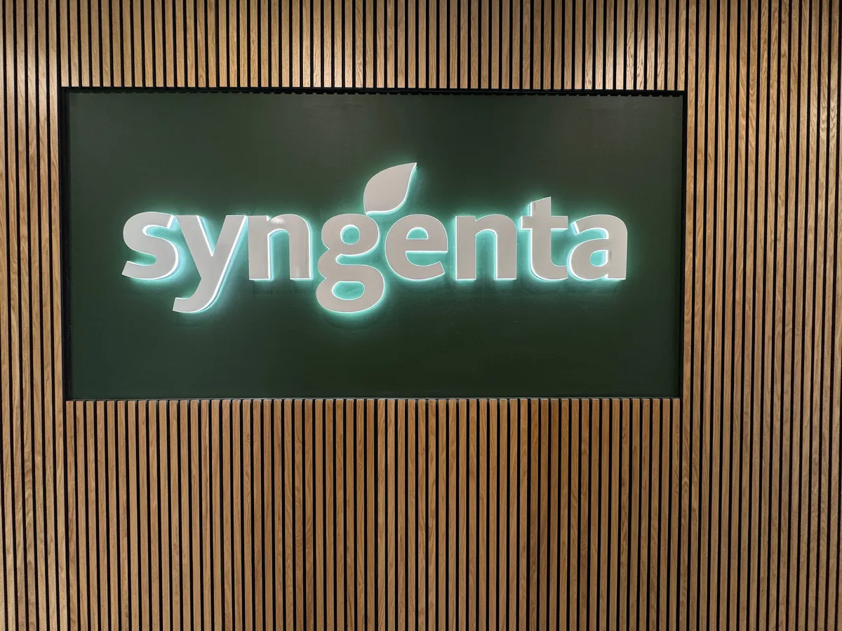 Verlicht syngenta-logo op een donker paneel tegen een houten lamellenwand