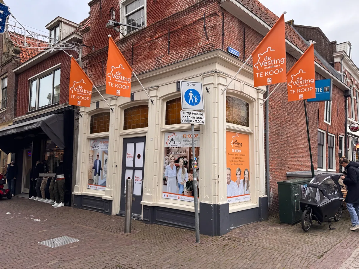Hoekpand met oranje vlaggen en raambeelden van de Vesting makelaars