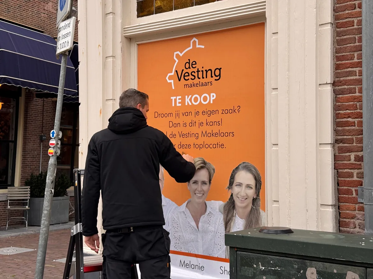 Monteur brengt het oranje raambeeld van de Vesting makelaars aan
