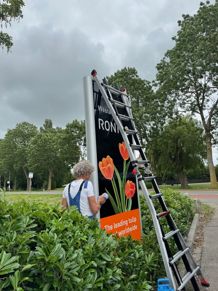 Monteur op een ladder werkt de reclamezuil van Ronico af