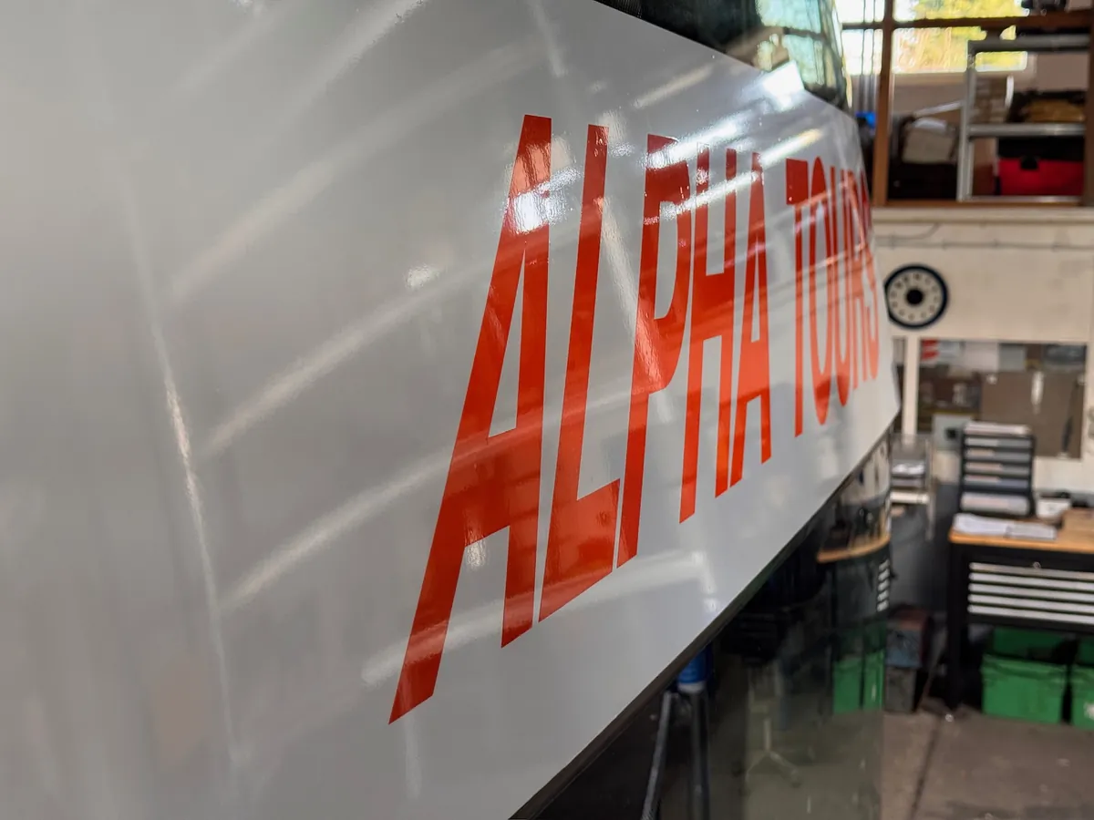 Rode letters ALPHA TOURS op de witte bus, schuin van dichtbij