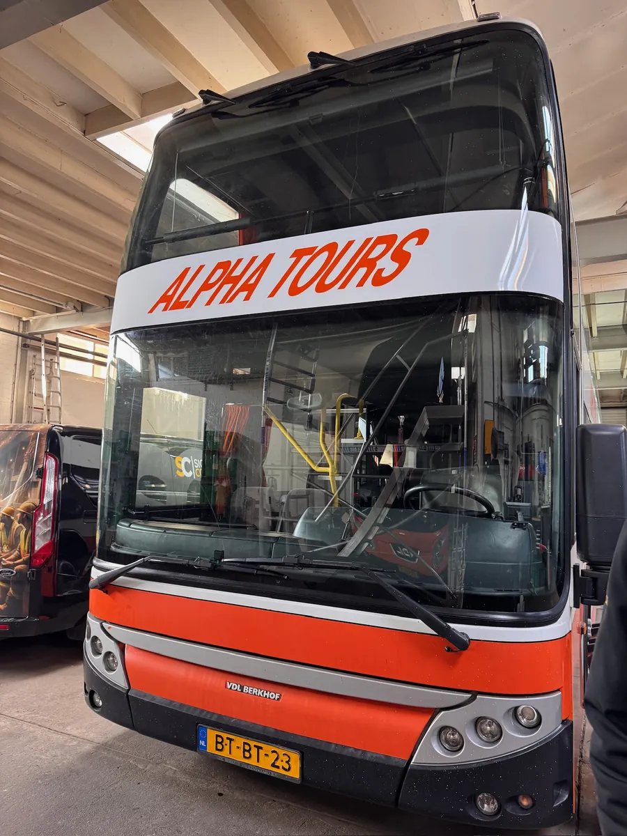 Voorkant van een dubbeldekker met de rode belettering ALPHA TOURS boven de voorruit