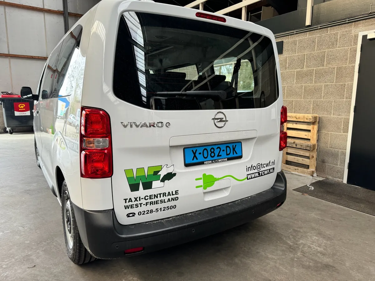 Achterkant van een witte bus met logo en gegevens van Taxi-Centrale West-Friesland