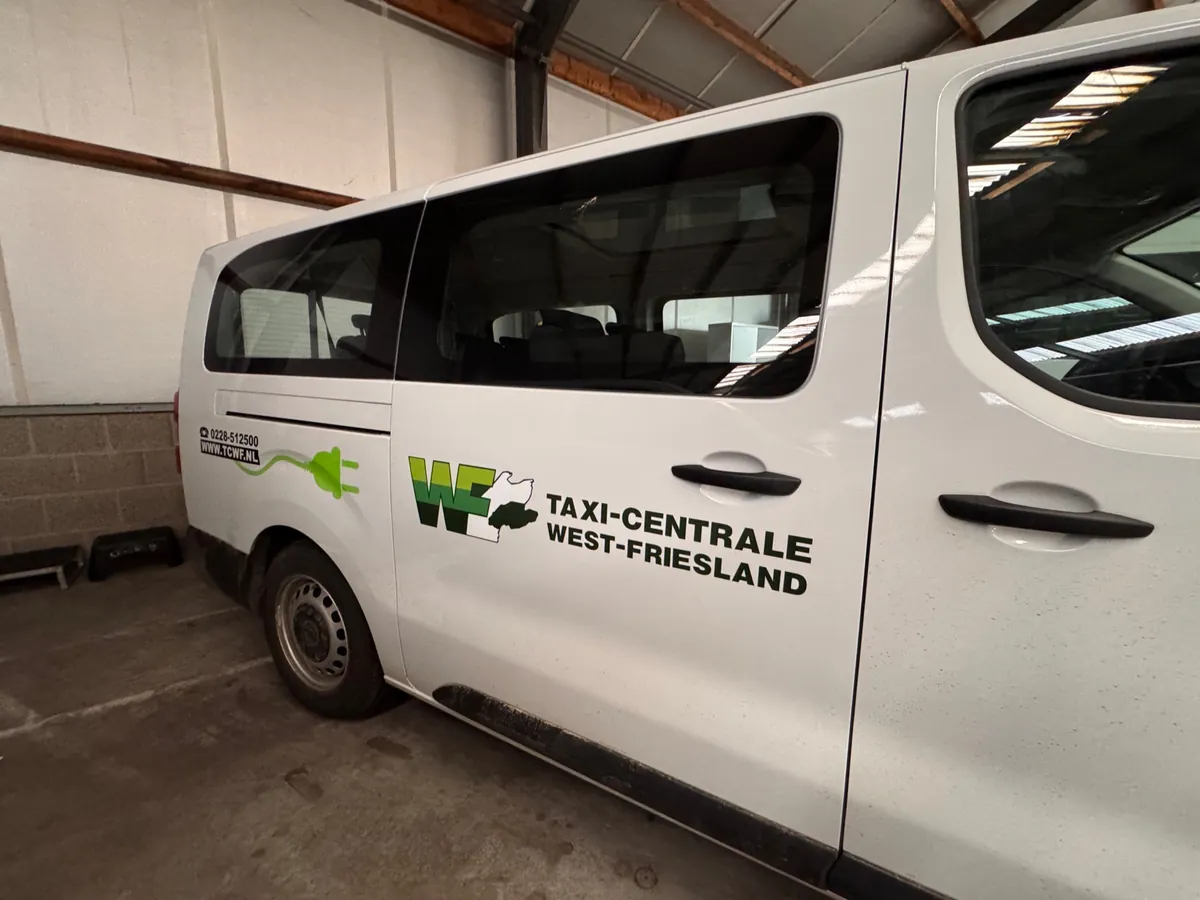 Flank van een witte bus met het logo van Taxi-Centrale West-Friesland
