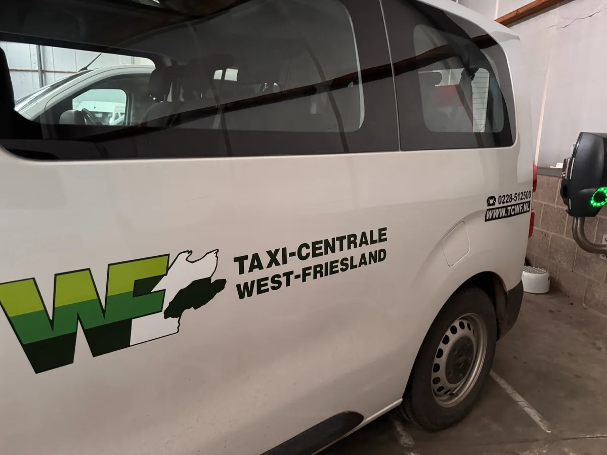 Witte bus met het groene logo van Taxi-Centrale West-Friesland op de zijkant