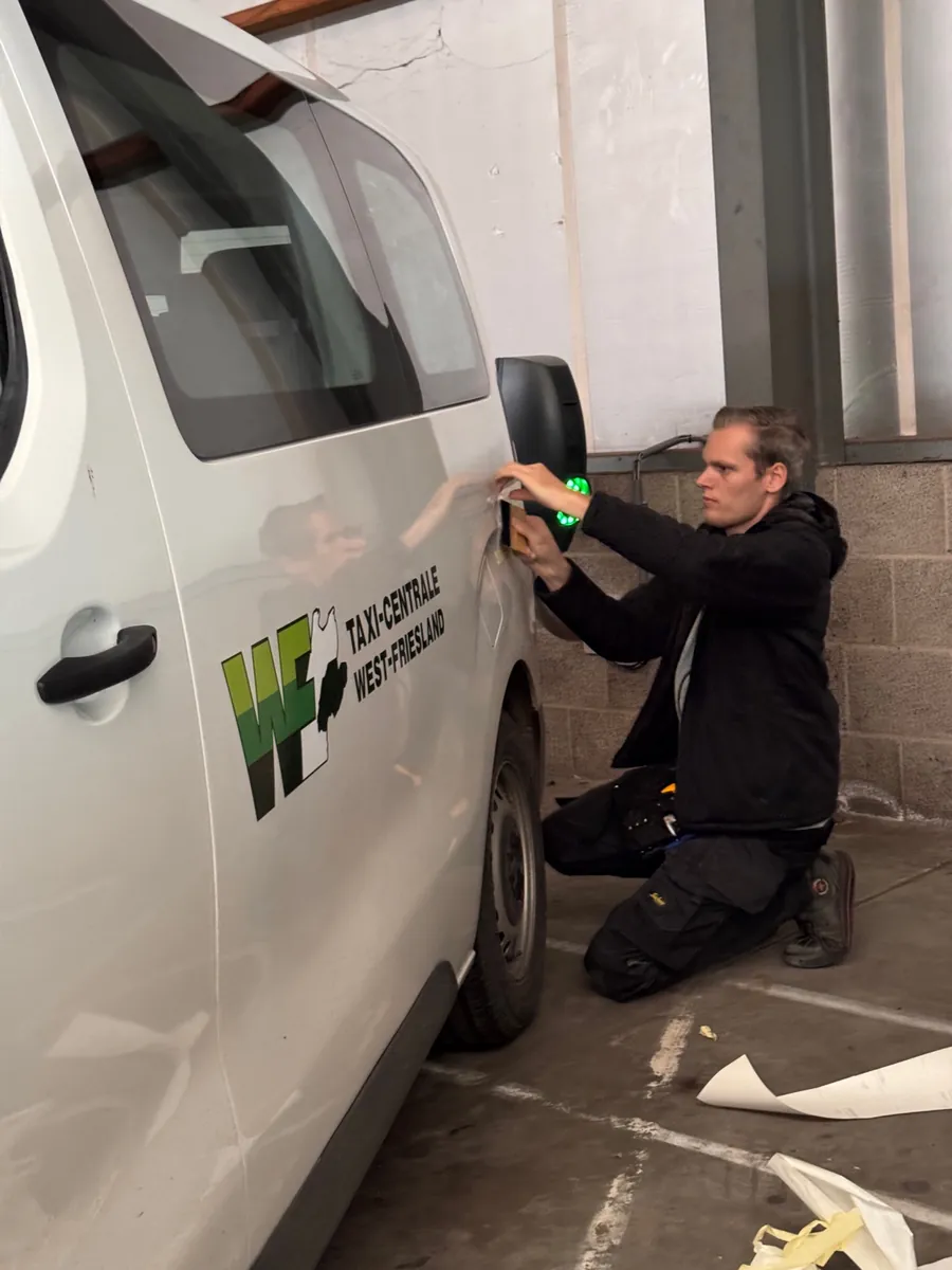 Monteur zit op zijn knieën bij de schuifdeur en brengt het logo van Taxi-Centrale West-Friesland aan