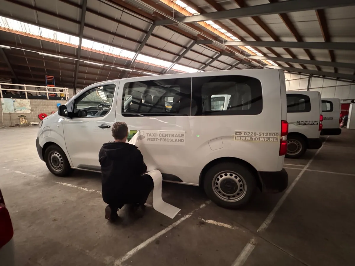 Monteur brengt belettering aan op de flank van een witte bus